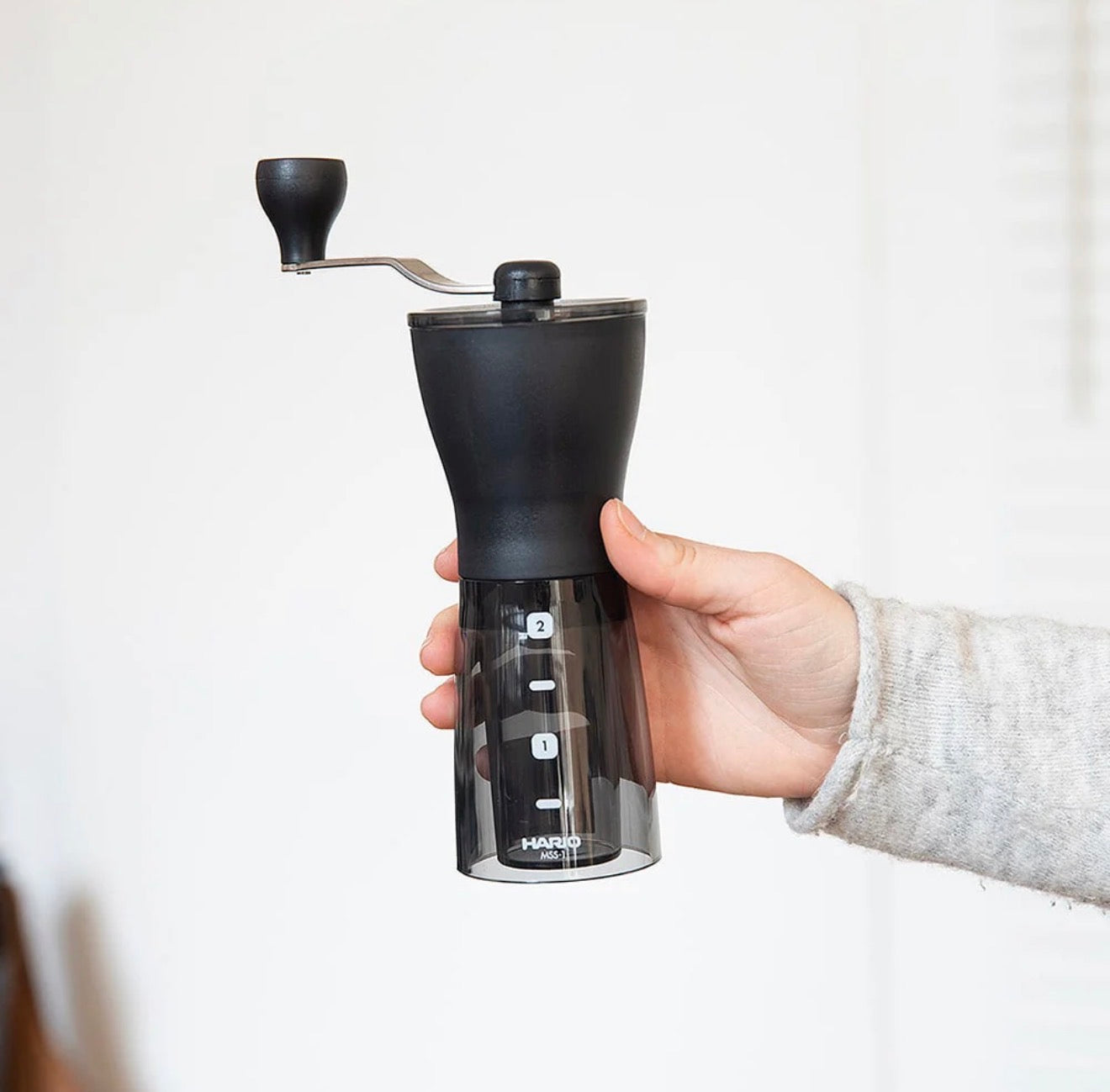 Hand holding a black Hario coffee grinder against a white background