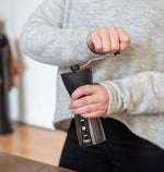 Person using a manual coffee grinder with a blurred background